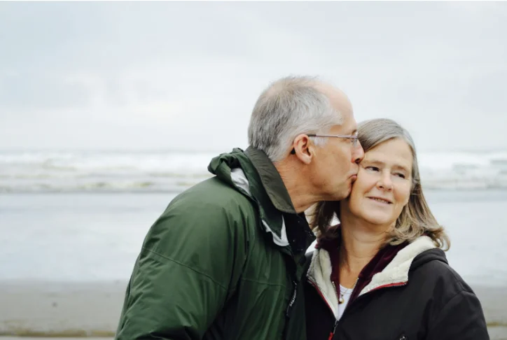 A middle-aged couple dealing with menopause changes sitting closely on a couch, holding hands and talking with care and understanding.