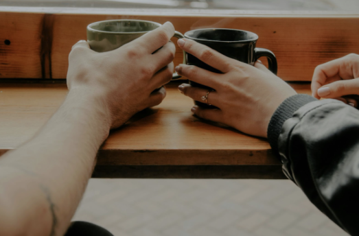 A happy couple sitting together at a cozy café in Portland, Oregon, holding hands and laughing while enjoying coffee on a rainy day after couples therapy.